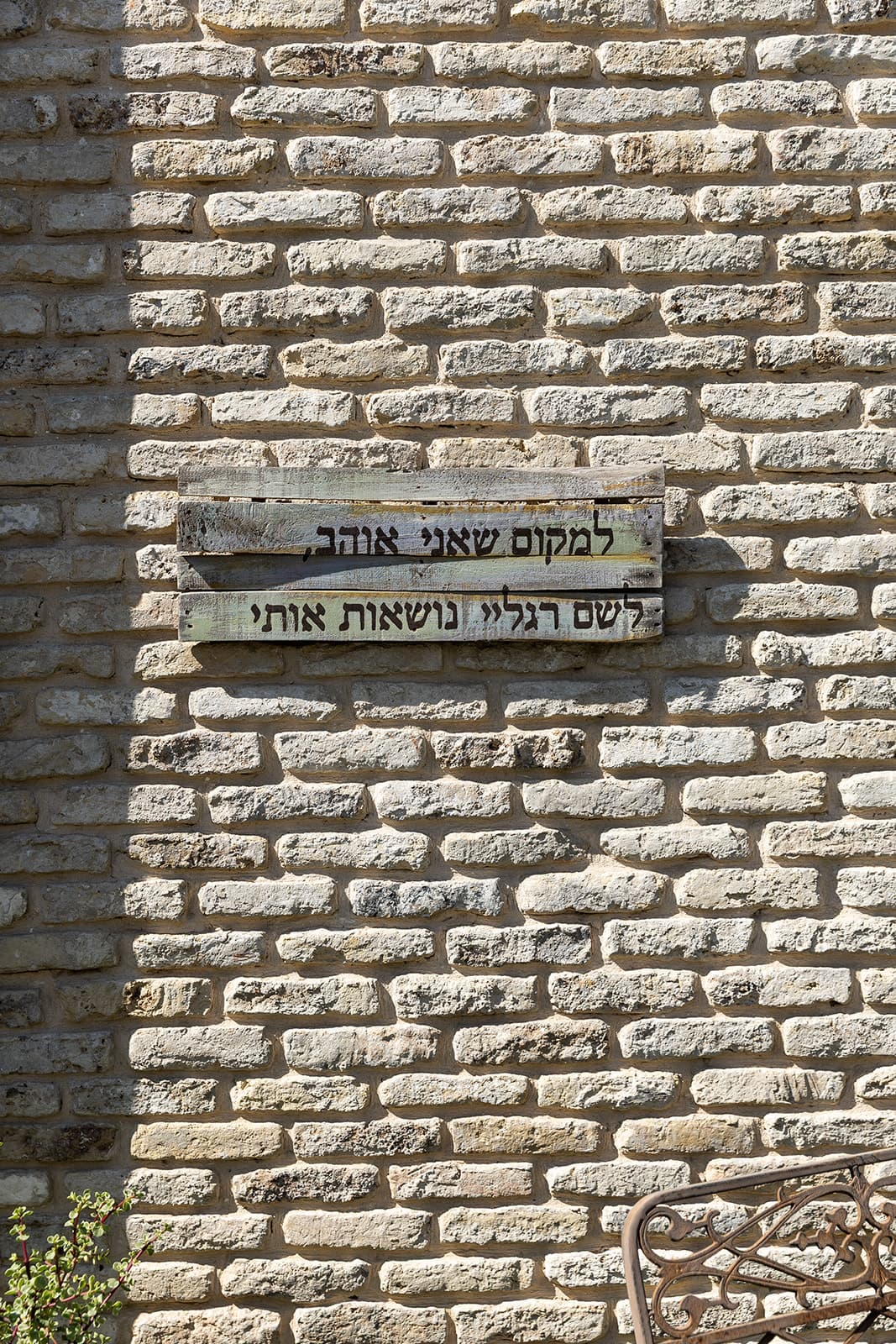 שלט עץ על קיר הלבנים: למקום שאני אוהב, לשם רגליי נושאות אותי